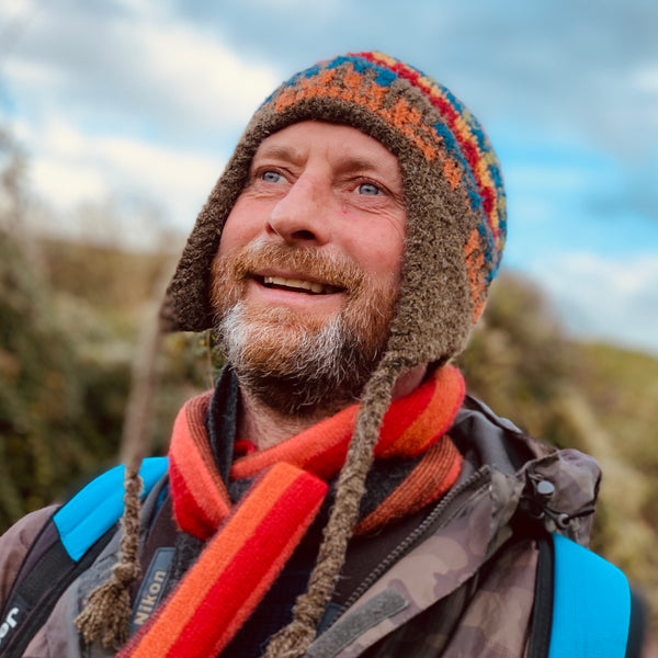 A man smiling in a striped alpaca chullo hat with ear flaps and an orange striped scarf