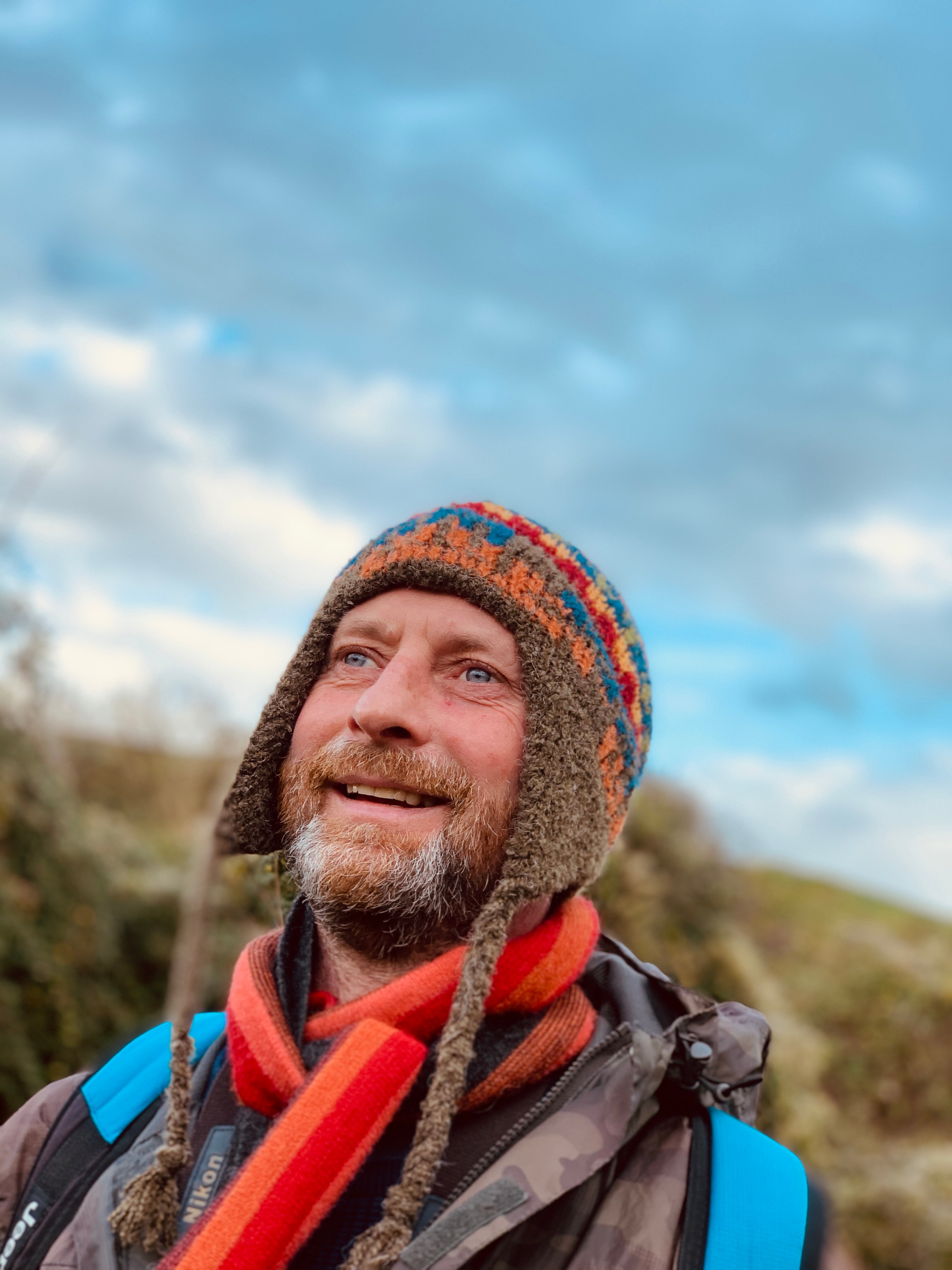 A man smiling in a striped alpaca chullo hat with ear flaps and an orange striped scarf