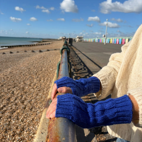 Blue cable knit alpaca gloves on a seafront railing, beach huts behind