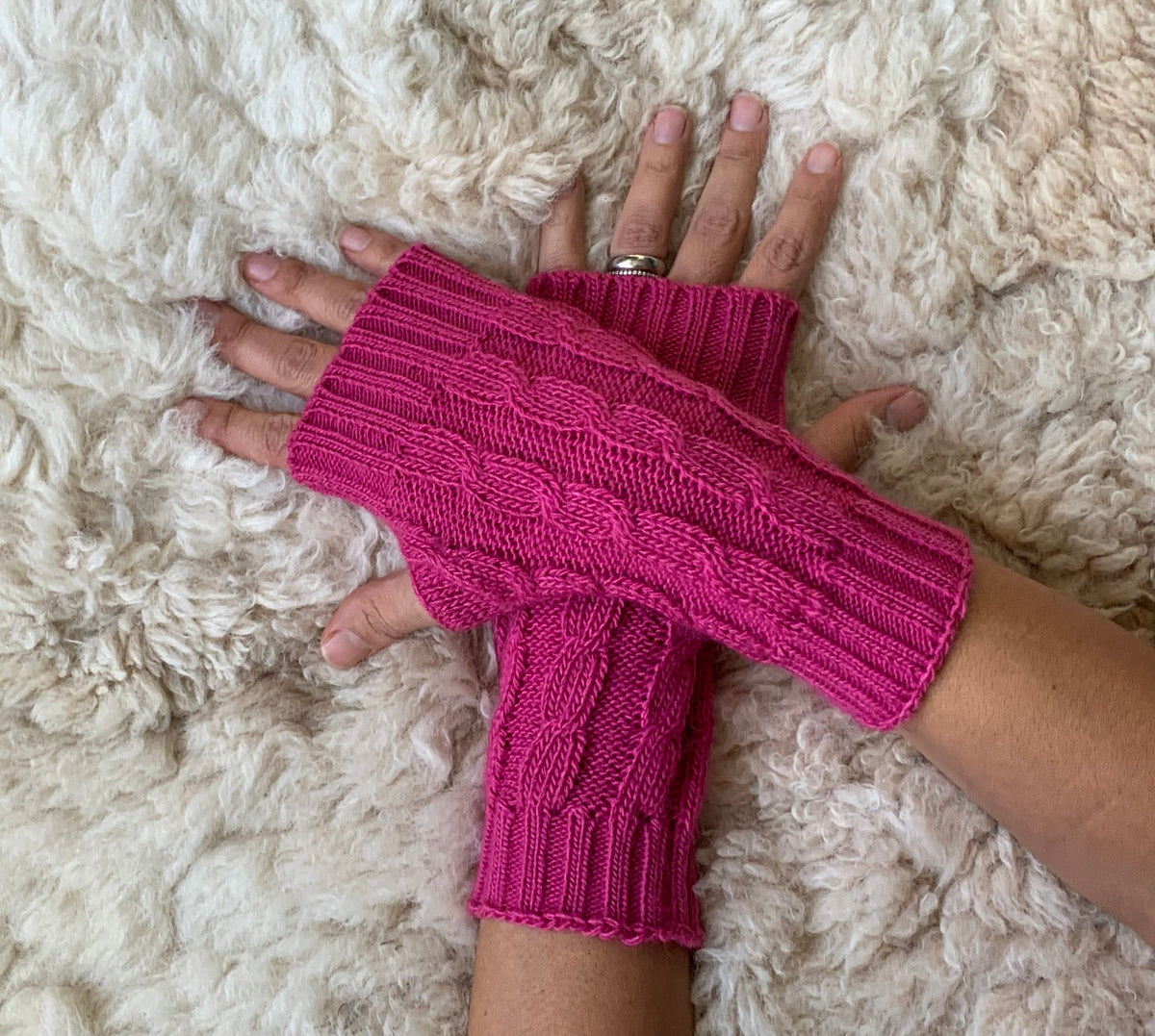 Cable Knit Alpaca Fingerless Gloves worn on hands resting on a sheepskin rug