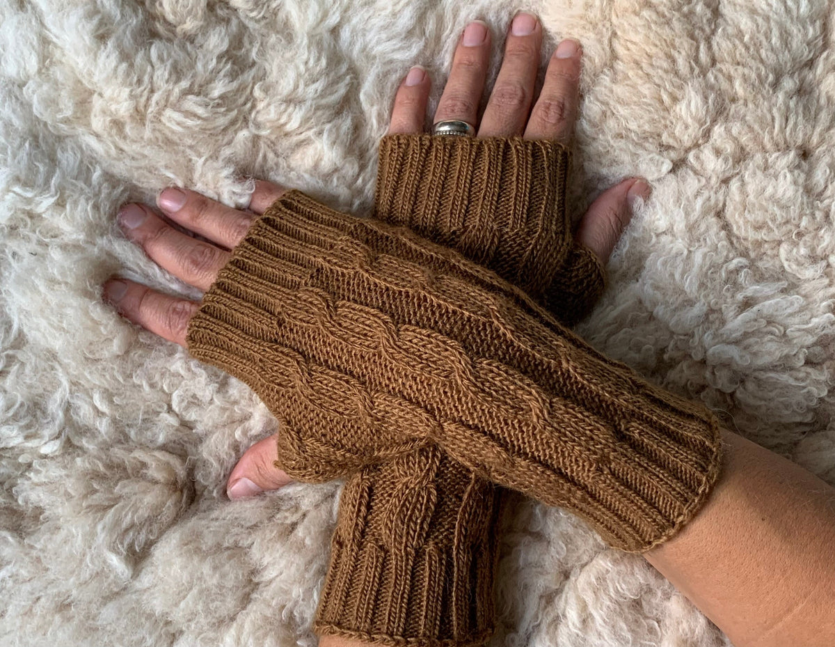 Caramel Cable Knit Alpaca Fingerless Gloves worn on hands resting on a sheepskin rug