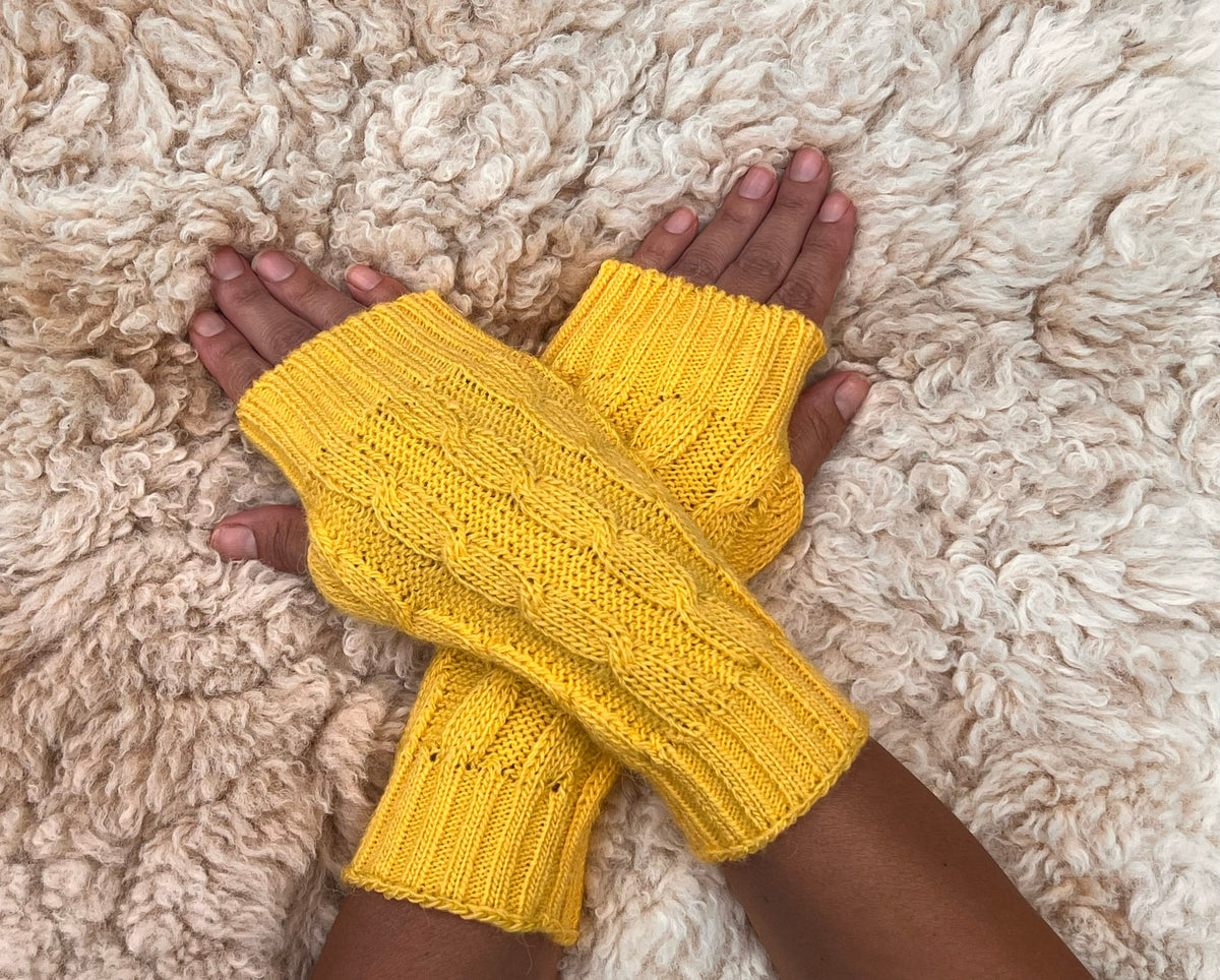 Sunshine Yellow Cable Knit Alpaca Fingerless Gloves worn on hands resting on a sheepskin rug