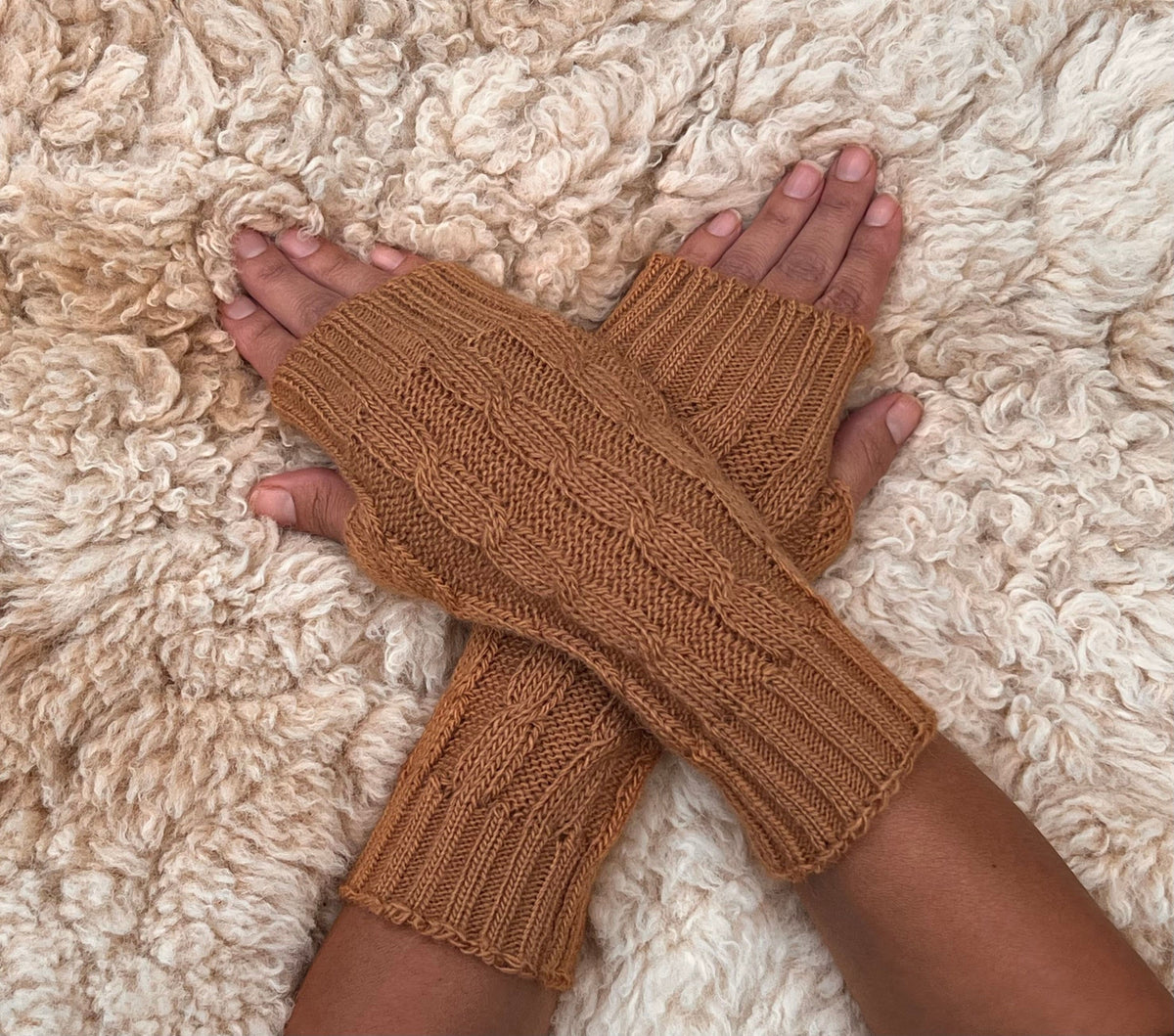 Caramel Cable Knit Alpaca Fingerless Gloves worn on hands resting on a sheepskin rug