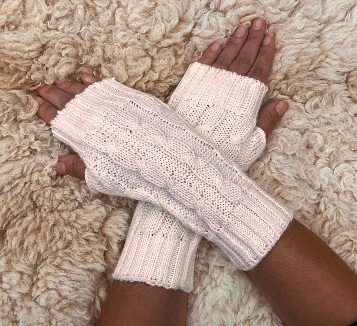 Ivory White Cable Knit Alpaca Fingerless Gloves worn on hands resting on a sheepskin rug