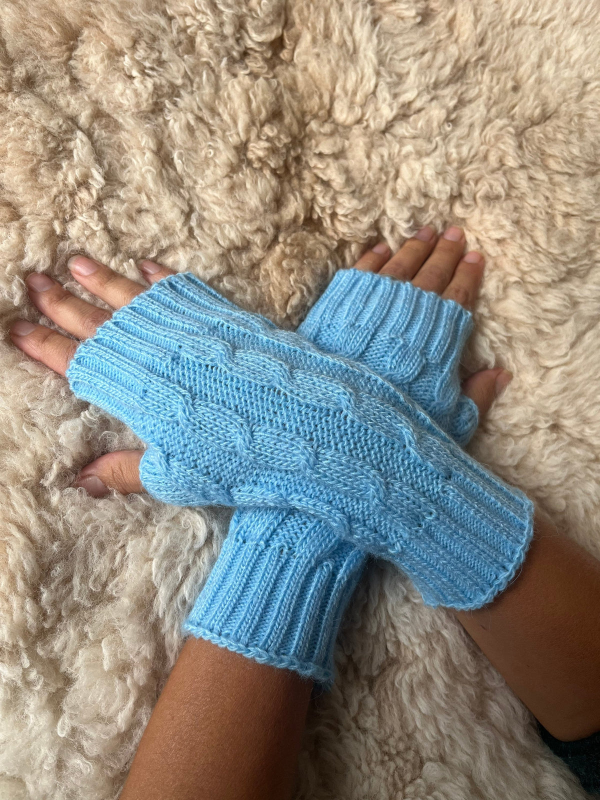 Baby Blue Cable Knit Alpaca Fingerless Gloves worn on hands resting on a sheepskin rug