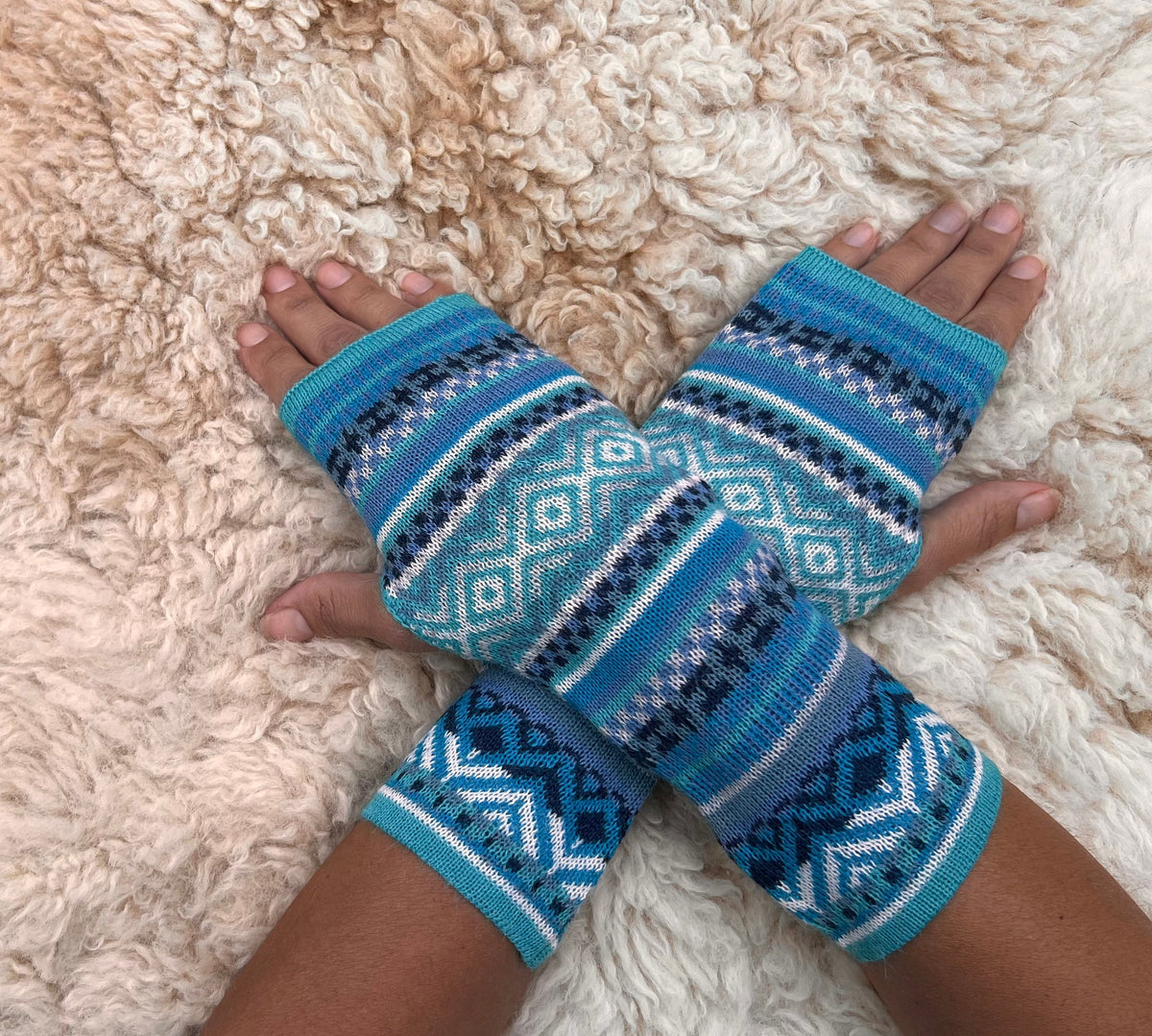 Aqua & Teal Fair Isle Baby Alpaca Fingerless Gloves worn on hands resting on a sheepskin rug