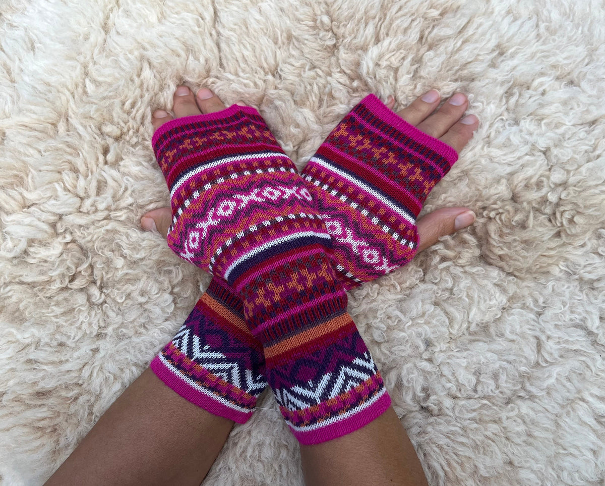 Magenta & Burgundy Fair Isle Baby Alpaca Fingerless Gloves worn on hands resting on a sheepskin rug