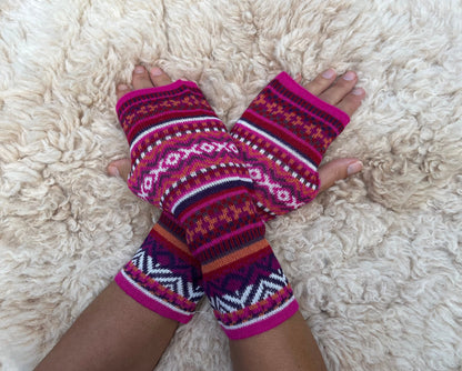 Magenta & Burgundy Fair Isle Baby Alpaca Fingerless Gloves worn on hands resting on a sheepskin rug