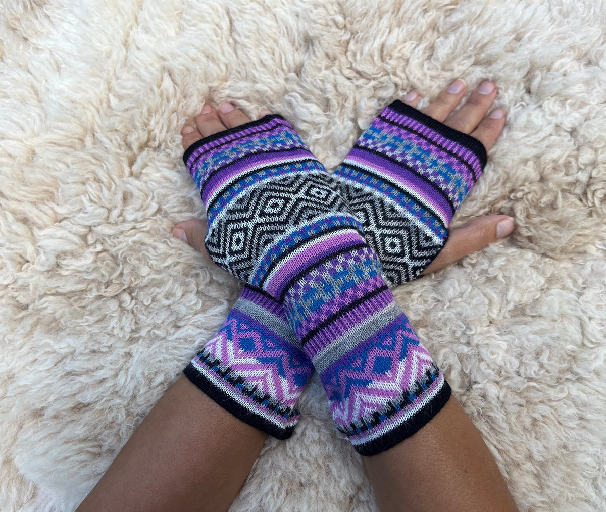 Lilac & Black Fair Isle Baby Alpaca Fingerless Gloves worn on hands resting on a sheepskin rug