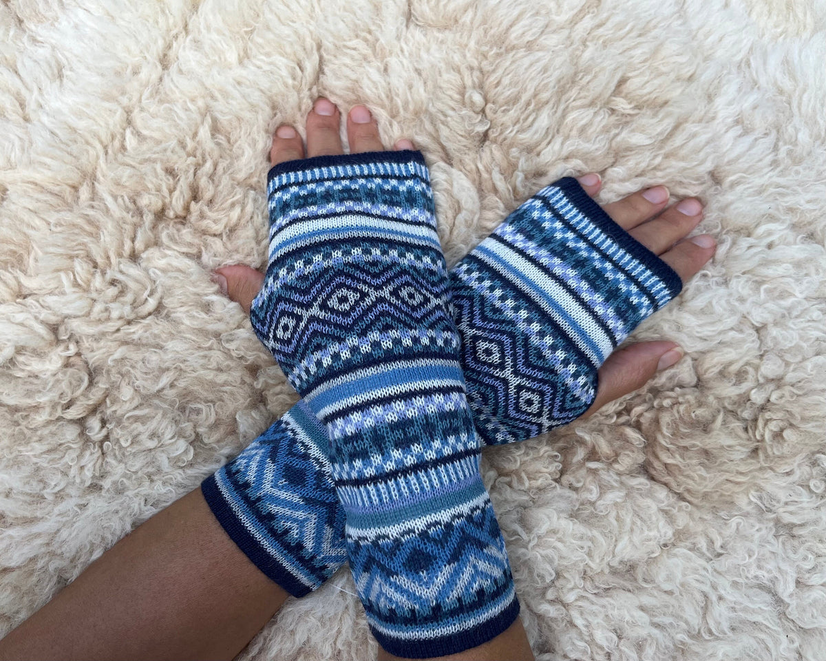 Fair Isle Baby Alpaca Fingerless Gloves worn on hands resting on a sheepskin rug