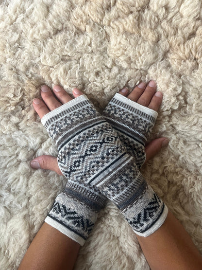 Grey & Taupe Fair Isle Baby Alpaca Fingerless Gloves worn on hands resting on a sheepskin rug