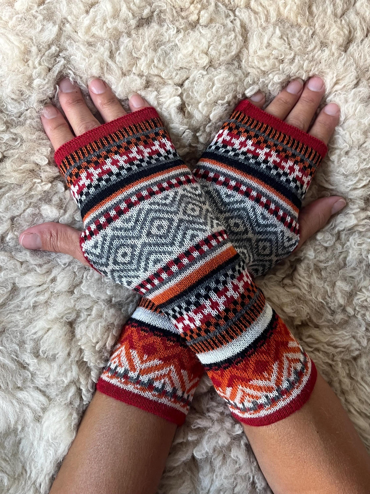 Fair Isle Baby Alpaca Fingerless Gloves worn on hands resting on a sheepskin rug