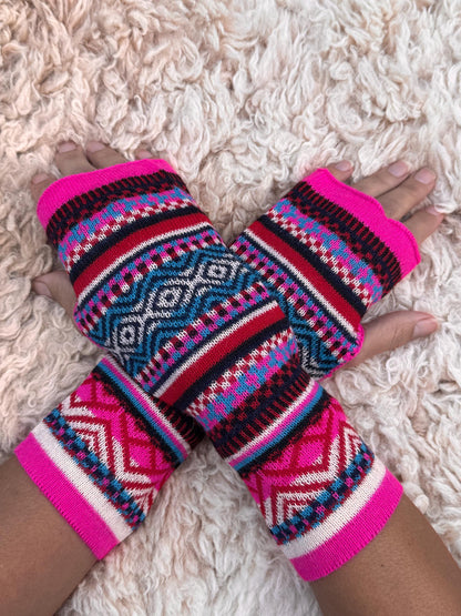 Neon Pink & Teal Fair Isle Baby Alpaca Fingerless Gloves worn on hands resting on a sheepskin rug