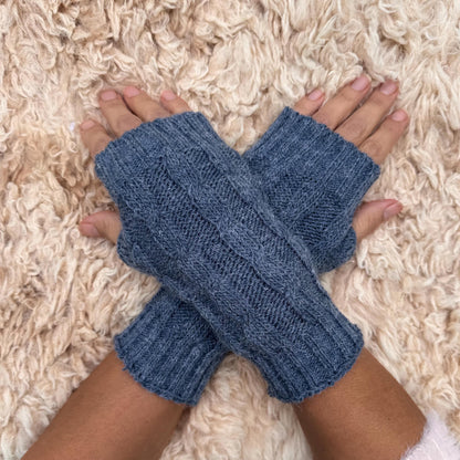 Denim Blue Cable Knit Alpaca Fingerless Gloves worn on hands resting on a sheepskin rug