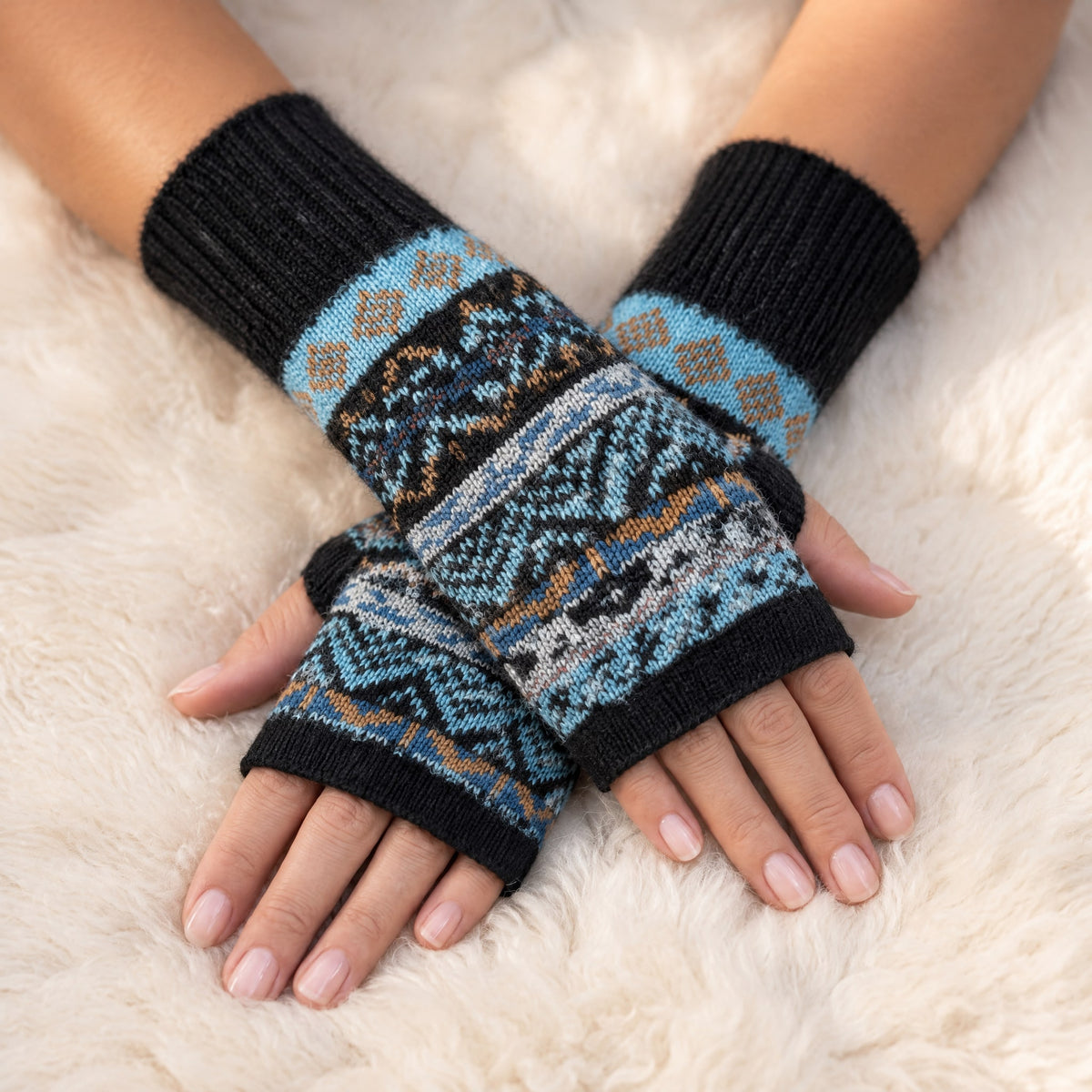 Black & Blue Fair Isle Alpaca Fingerless Gloves worn on hands resting on a sheepskin rug