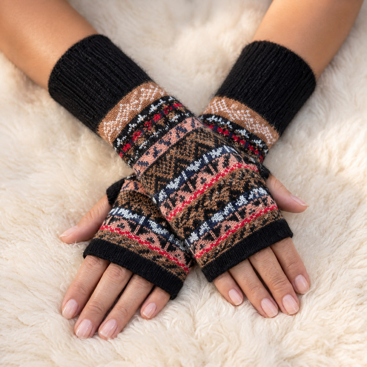 Black & Peach Fair Isle Alpaca Fingerless Gloves worn on hands resting on a sheepskin rug