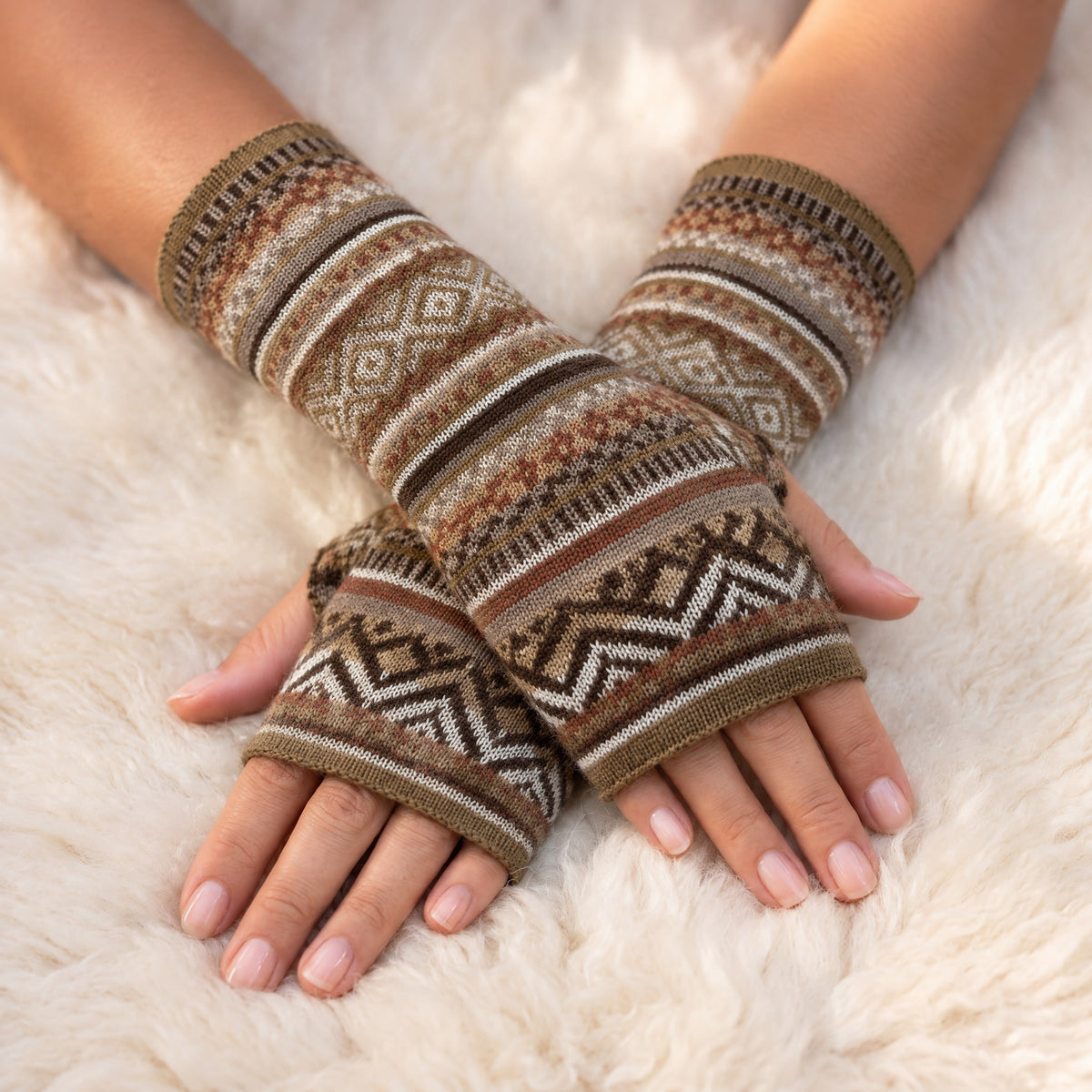 Camel & Cream Fair Isle Baby Alpaca Fingerless Gloves worn on hands resting on a sheepskin rug