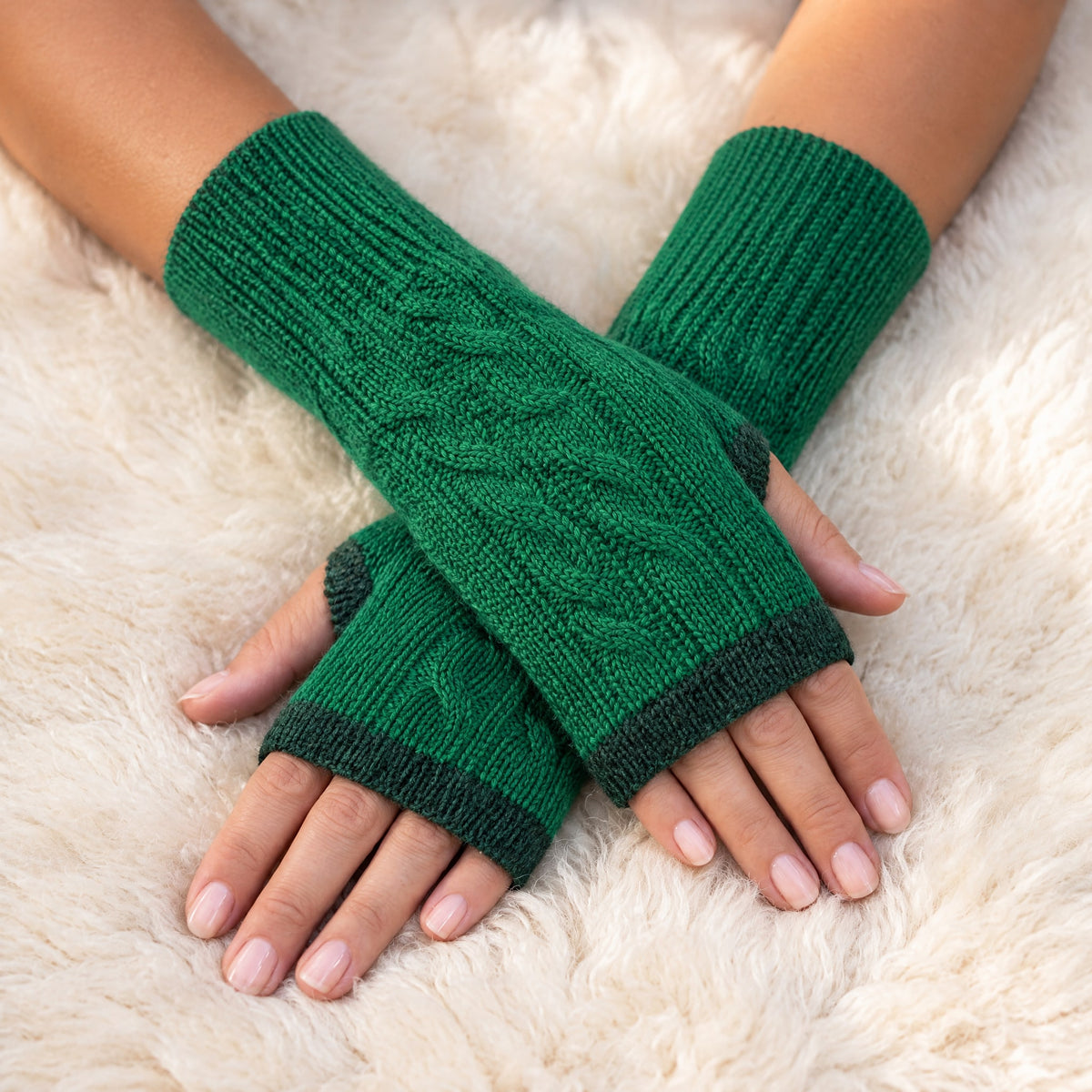 Emerald Green Reversible Cable Knit Baby Alpaca Fingerless Gloves worn on hands resting on a sheepskin rug