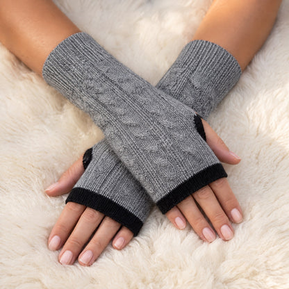 Grey & Black Reversible Cable Knit Baby Alpaca Fingerless Gloves worn on hands resting on a sheepskin rug