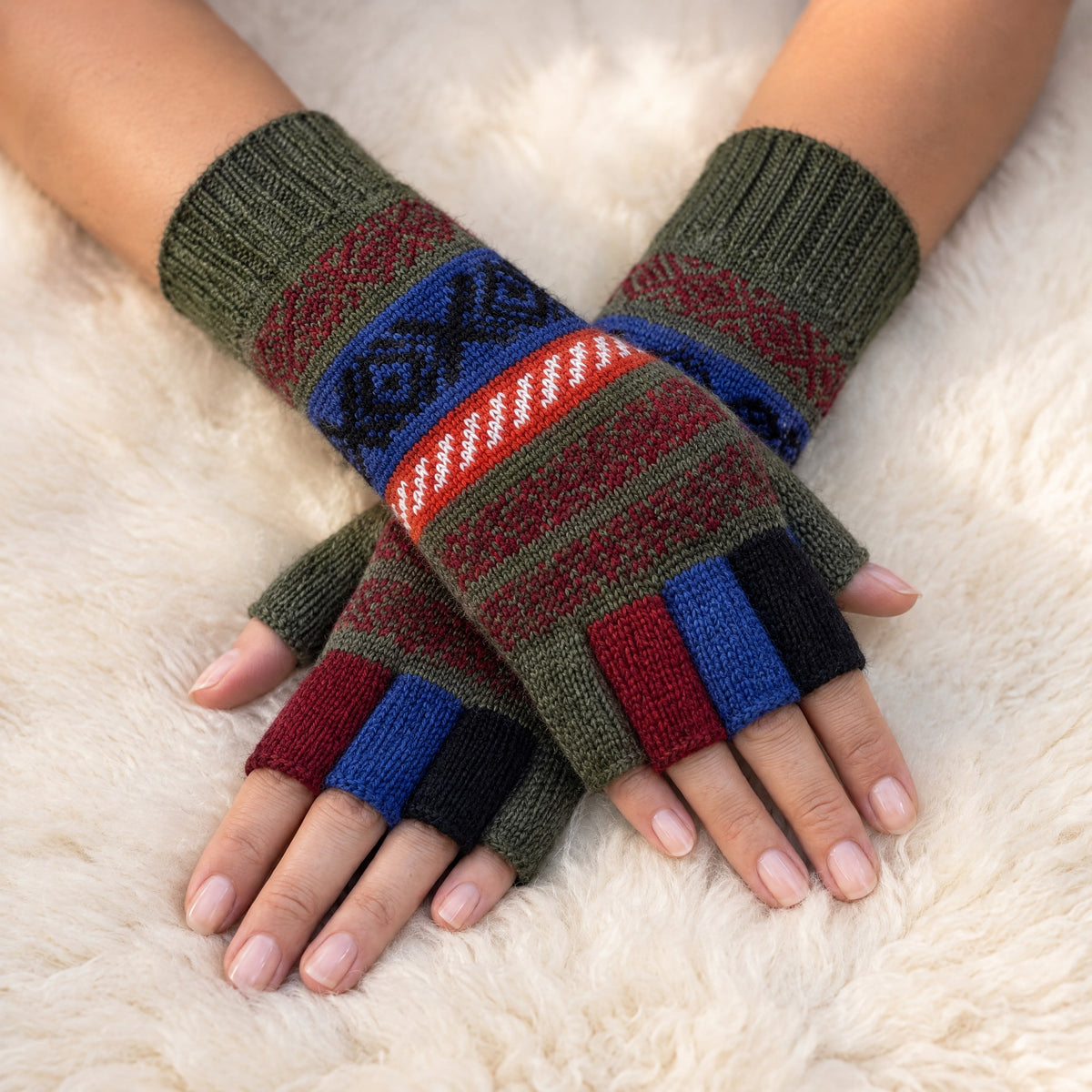 Olive Green Andean Fair Isle Half-Finger Alpaca Gloves worn on hands resting on a sheepskin rug