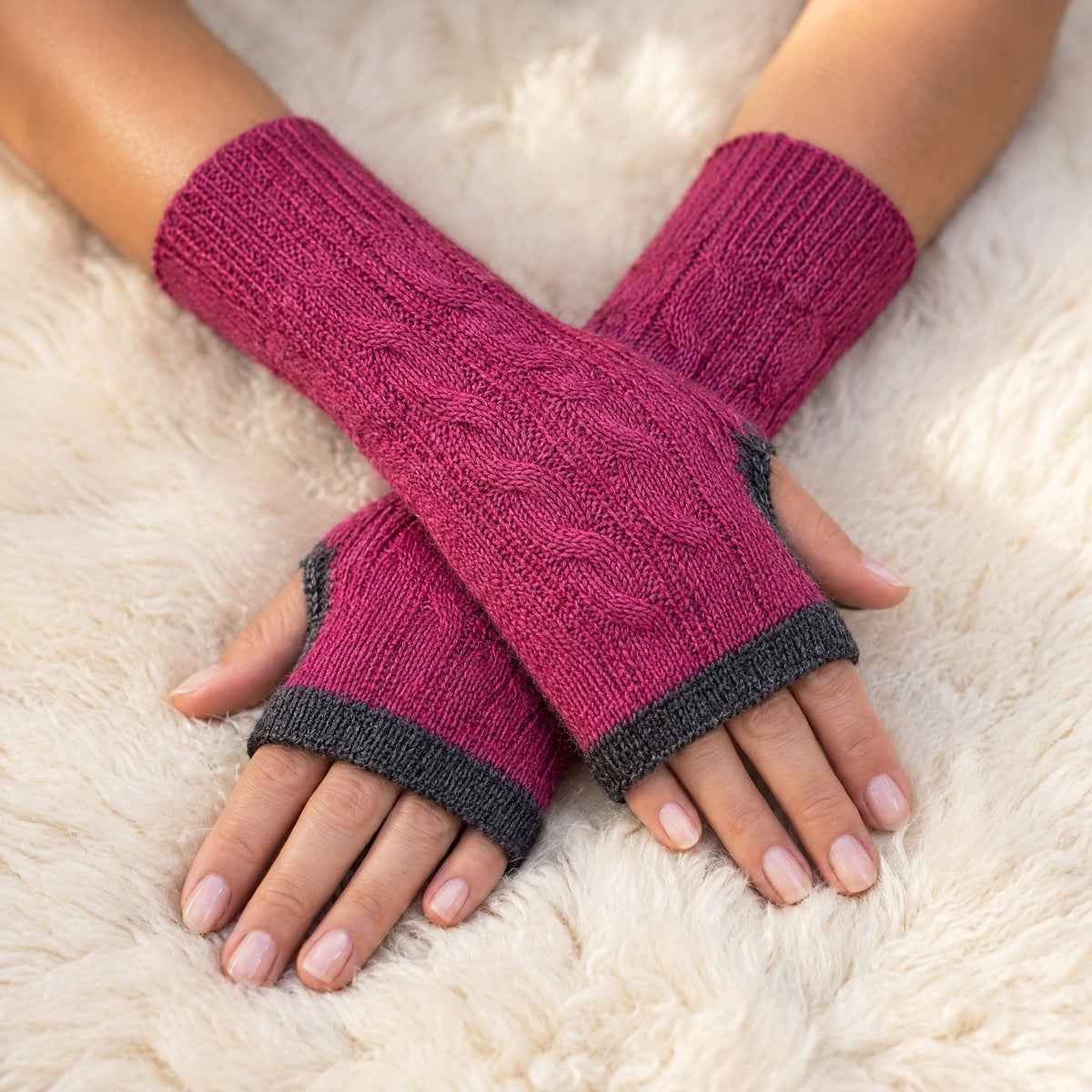 Pink & Grey Reversible Cable Knit Baby Alpaca Fingerless Gloves worn on hands resting on a sheepskin rug