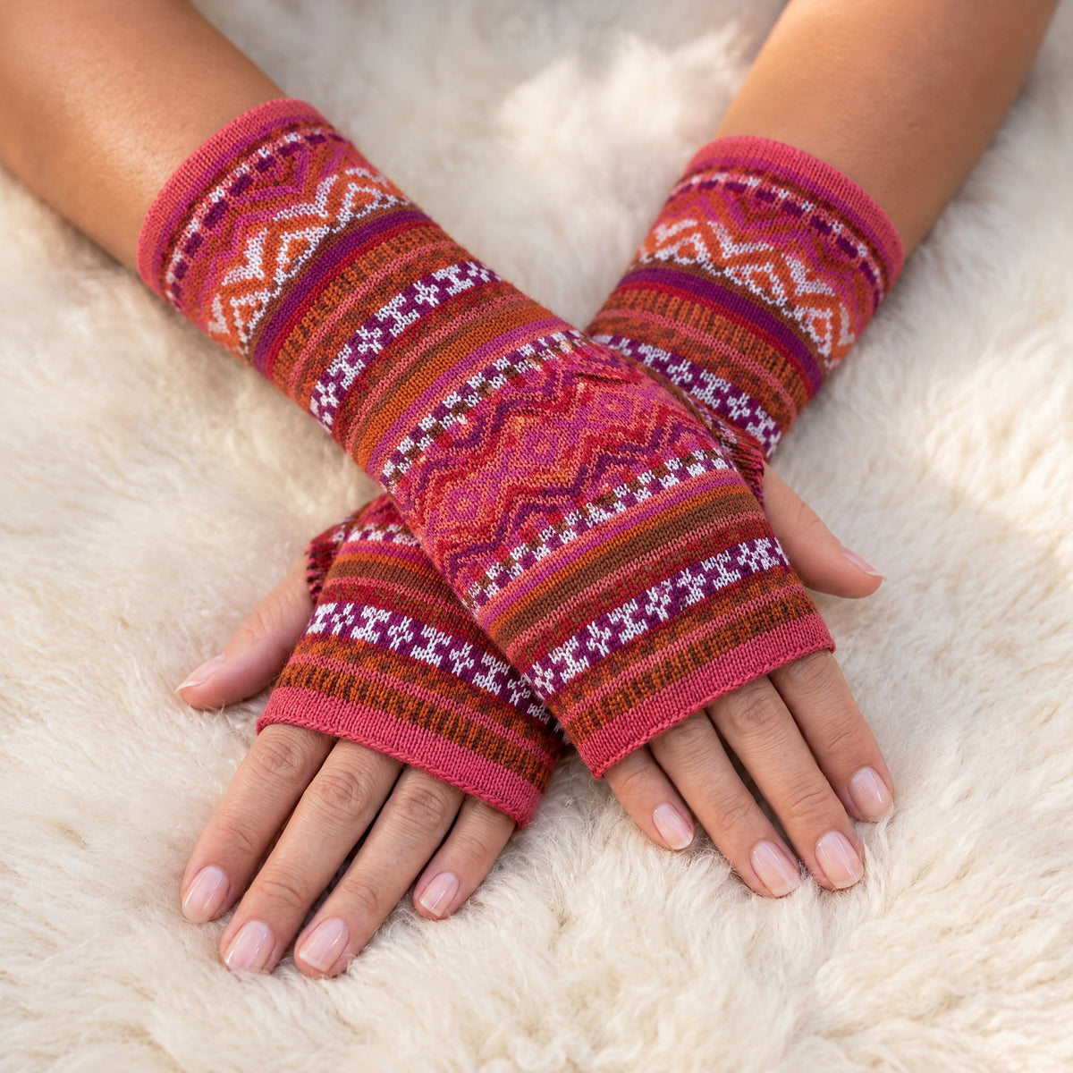 Pink & Orange Fair Isle Baby Alpaca Fingerless Gloves worn on hands resting on a sheepskin rug