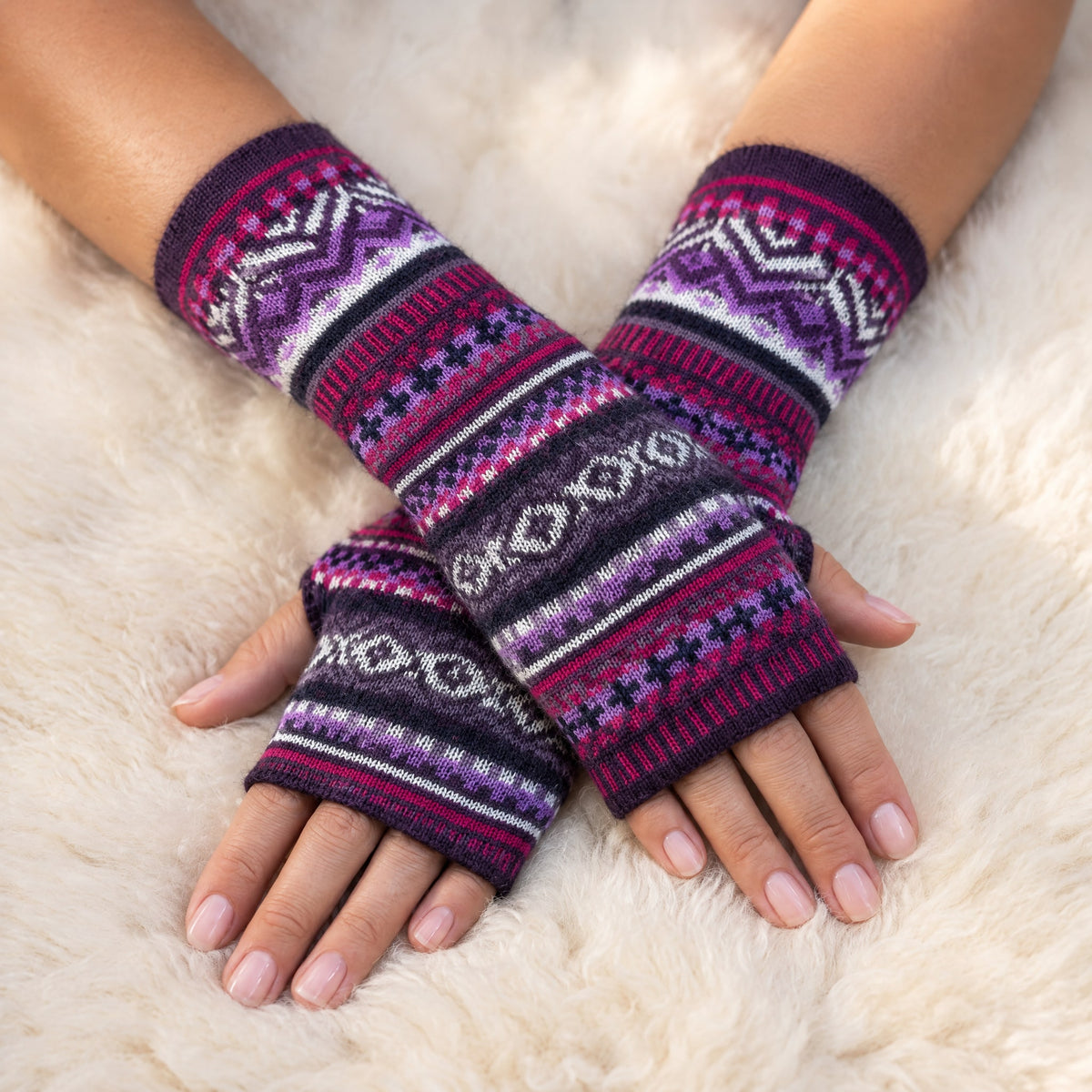 Plum & Magenta Fair Isle Baby Alpaca Fingerless Gloves worn on hands resting on a sheepskin rug