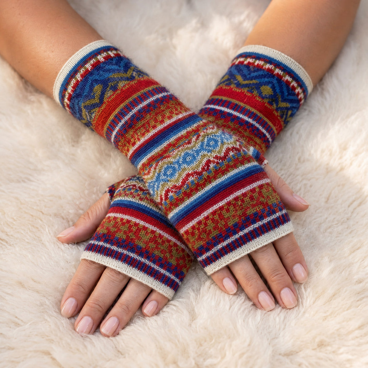 Red & Royal Blue Fair Isle Baby Alpaca Fingerless Gloves worn on hands resting on a sheepskin rug