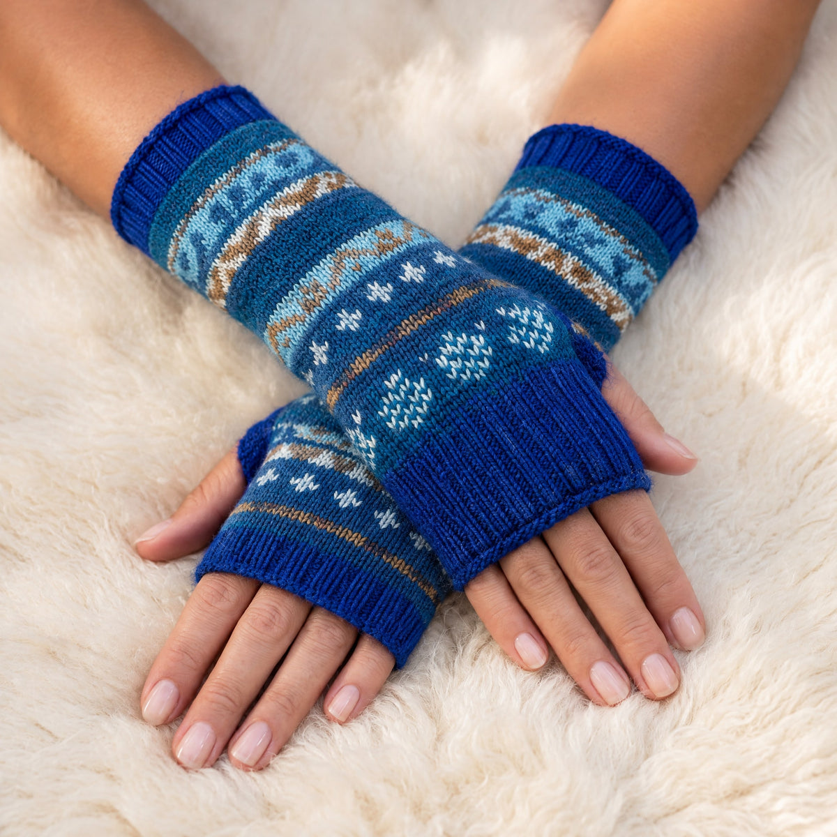 Royal Blue Fair Isle Alpaca Fingerless Gloves worn on hands resting on a sheepskin rug
