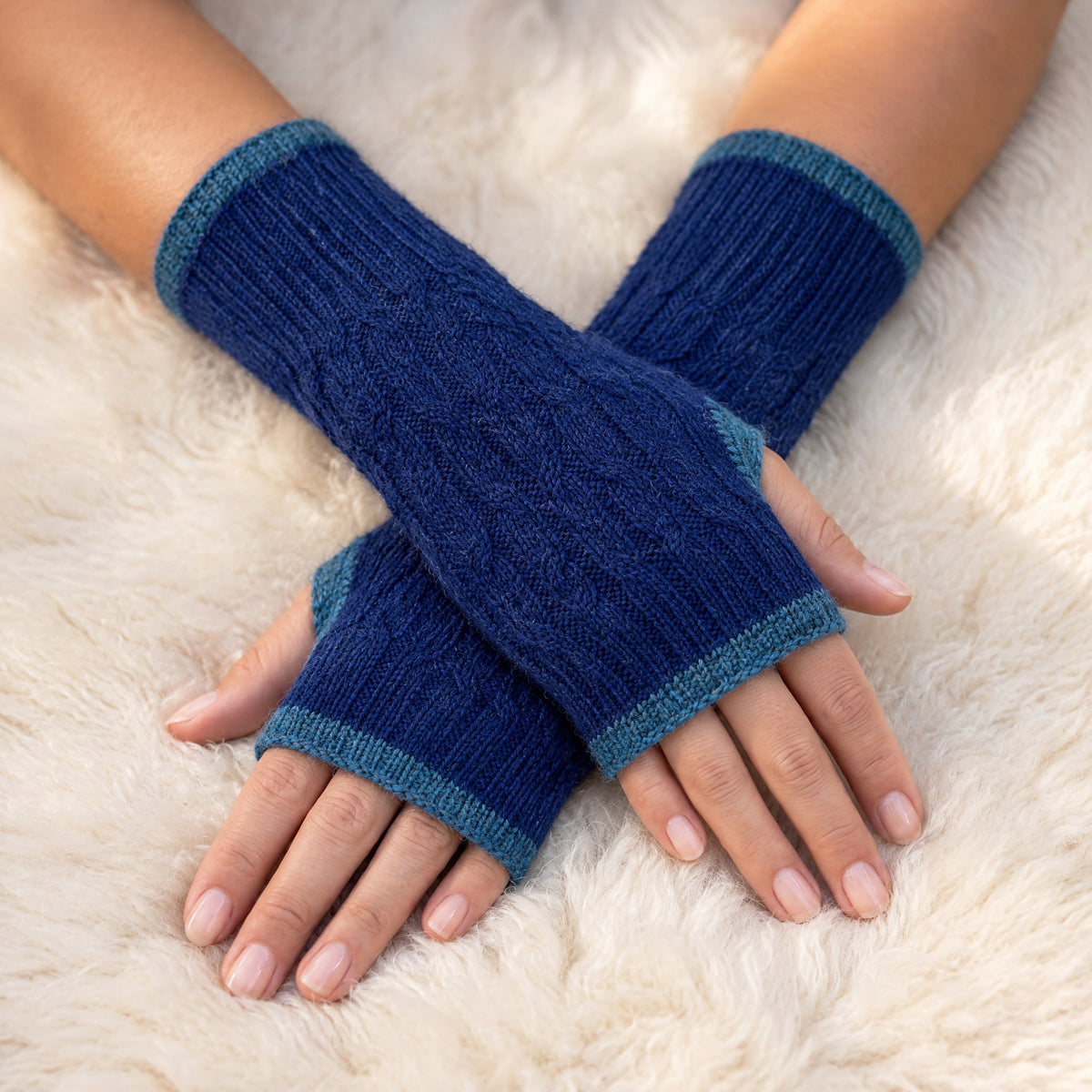 Royal Blue & Teal Reversible Cable Knit Baby Alpaca Fingerless Gloves worn on hands resting on a sheepskin rug