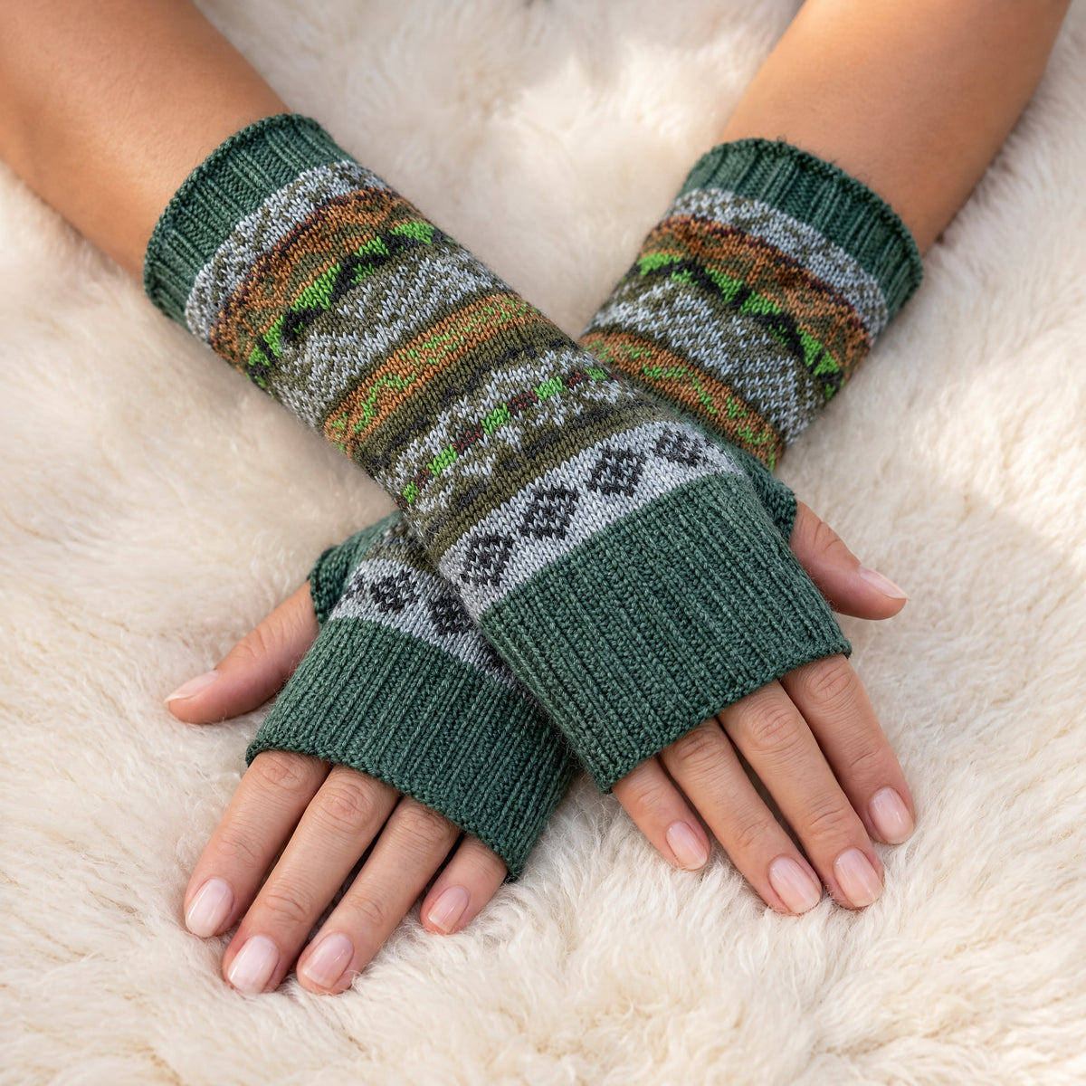 Sage Green Fair Isle Alpaca Fingerless Gloves worn on hands resting on a sheepskin rug