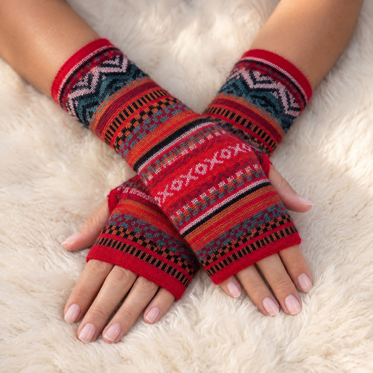 Scarlet Red Fair Isle Baby Alpaca Fingerless Gloves worn on hands resting on a sheepskin rug