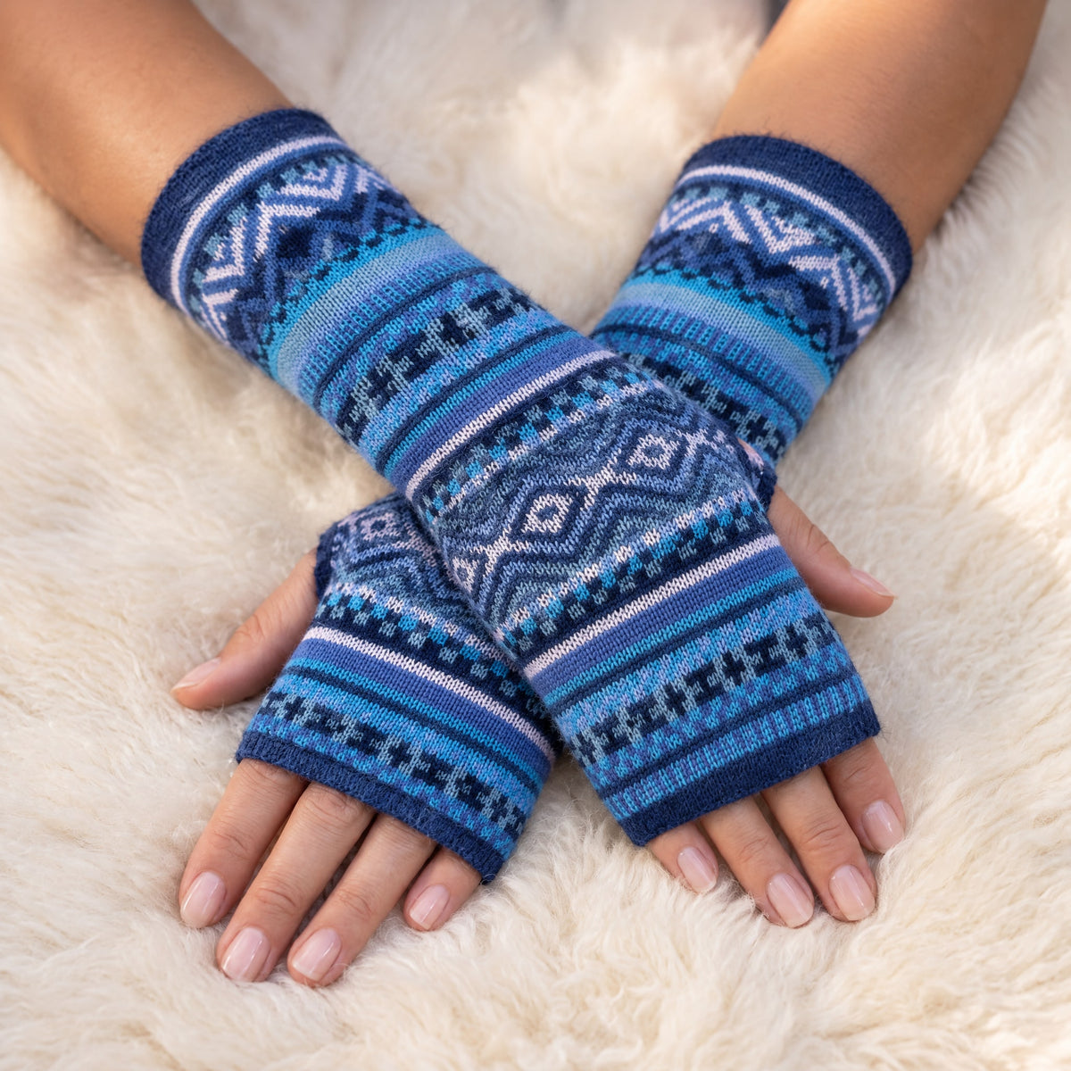 Sky Blue Fair Isle Baby Alpaca Fingerless Gloves worn on hands resting on a sheepskin rug