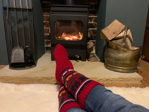 Feet in red llama alpaca socks by a lit wood burner